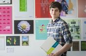 Student holding their portfolio in front of a wall of students' graphic design works 